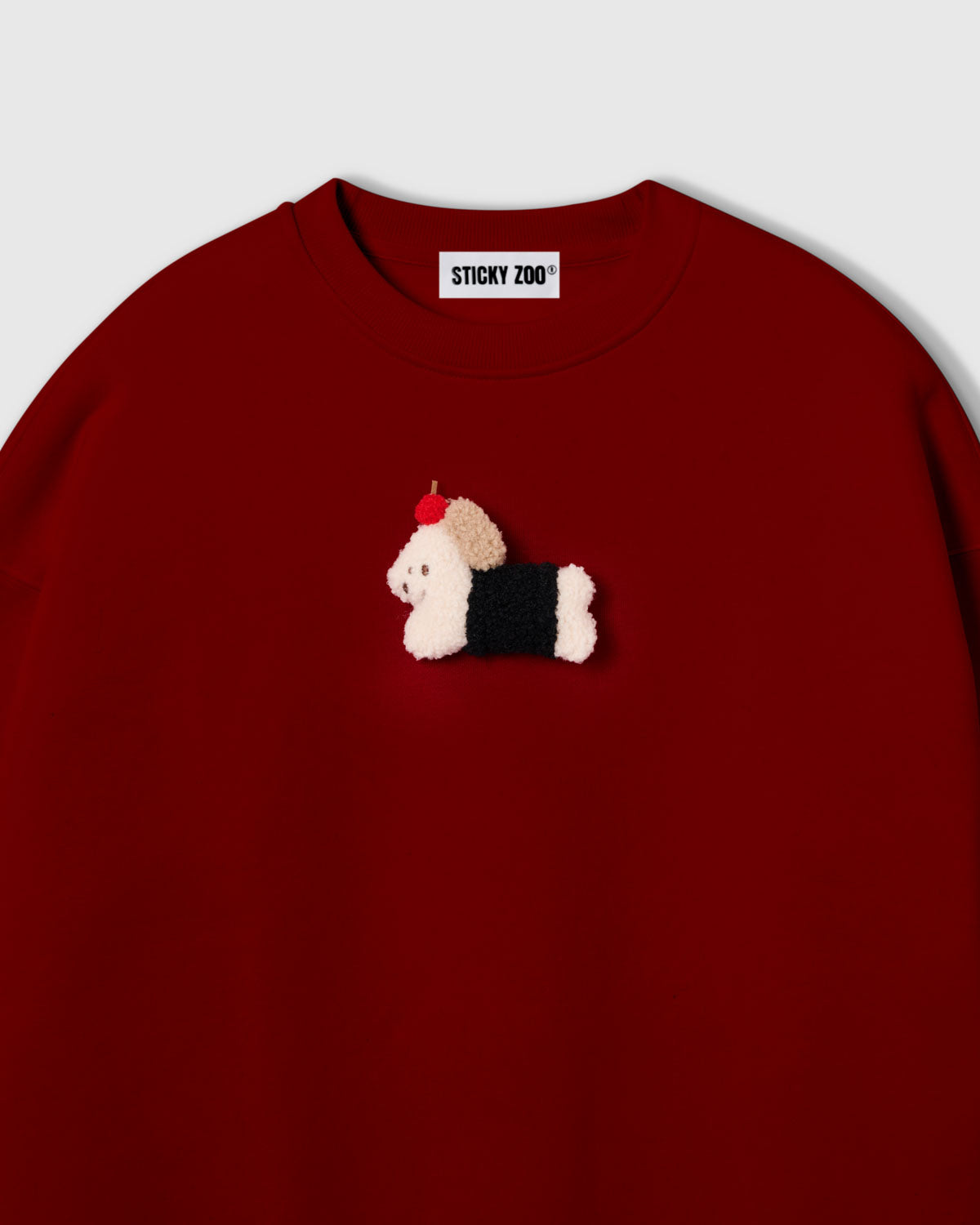 {{Not printed — stitched}} Close-up of plush dachshund in black coat with red apple on red cotton showing dimensional layered texture