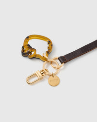 Close-up of tortoise acetate cat mirror charm showing layered amber and brown pattern with engraved STICKYZOO gold hardware