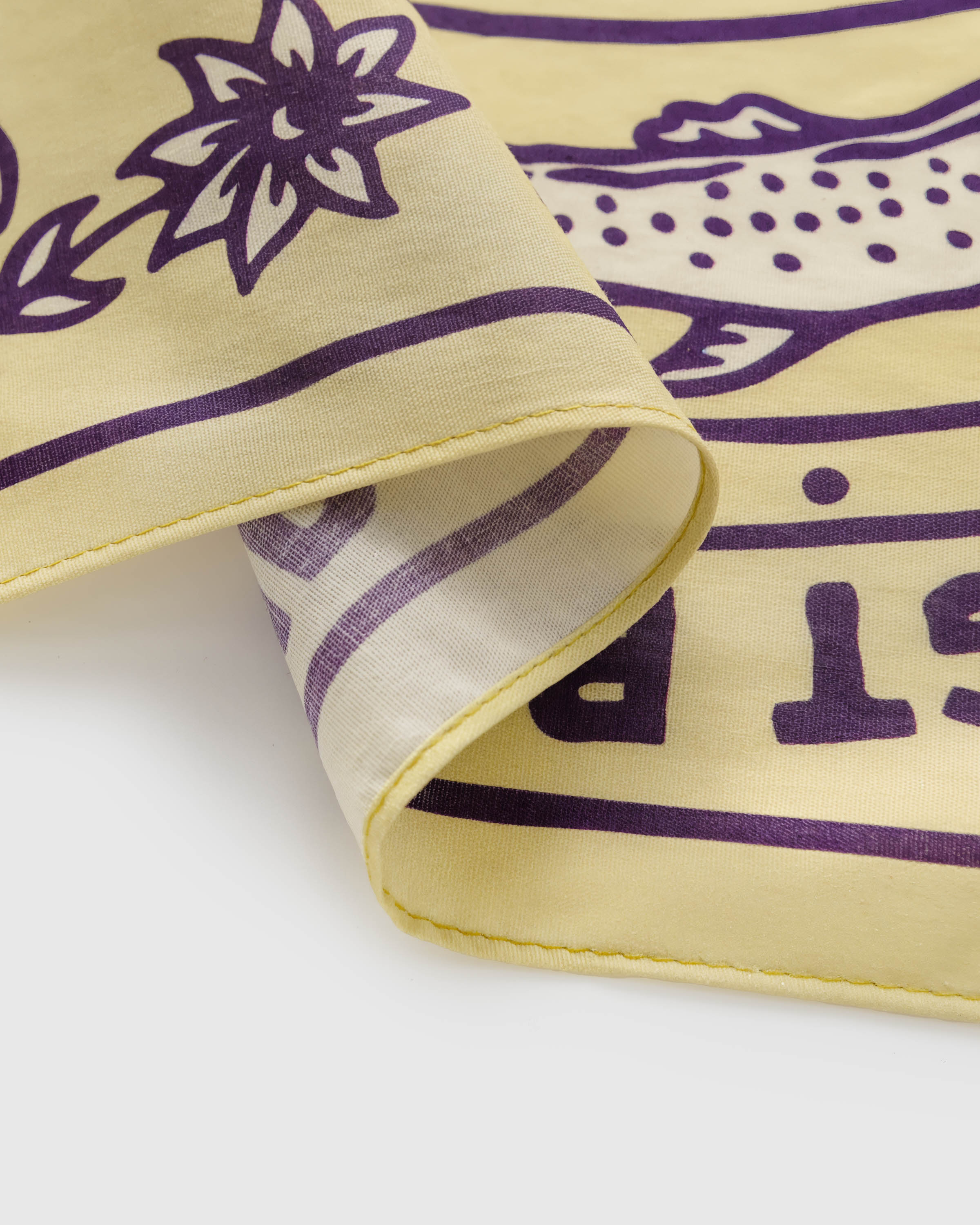 Folded edge of the yellow silk scarf showing the soft reverse and the aubergine printed motif