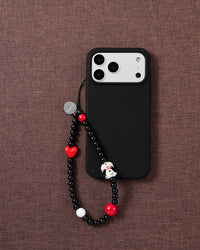 The beaded dalmatian phone strap looped on a black phone case over brown fabric, dalmatian puppy and red beads facing up.