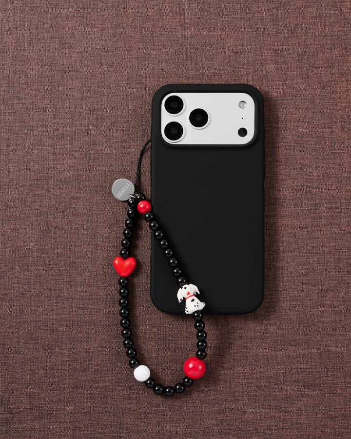 The beaded dalmatian phone strap looped on a black phone case over brown fabric, dalmatian puppy and red beads facing up.