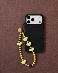 Lemon Heart beaded strap looped onto a black phone case on mauve fabric, pale yellow hearts and striped beads hanging free