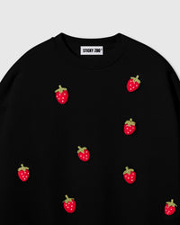 Close-up of plush strawberry with red body, white seeds, and green stem on black cotton showing stuffed 3D texture