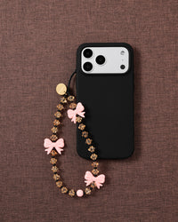 STICKYZOO bow strap looped onto a black phone case on mauve fabric, showing honey beads, black spacers and a round pink bead