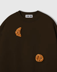 Close-up of crescent plush croissant on brown cotton showing tonal warmth and layered 3D texture