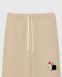 Close-up of hand-stitched plush dachshund with black coat and red apple on cream cotton sweatpants showing layered texture