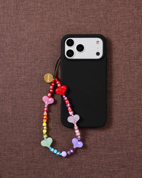 STICKYZOO rainbow jelly heart bead strap looped onto a black phone case on maroon fabric, hearts in red, pink, mint and lavender.