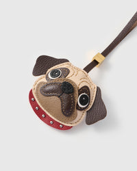 Close-up of The Pug Charm — hand-stitched wrinkle lines across the cream-beige face, dark brown layered muzzle, sparkly black nose. Every panel by hand.