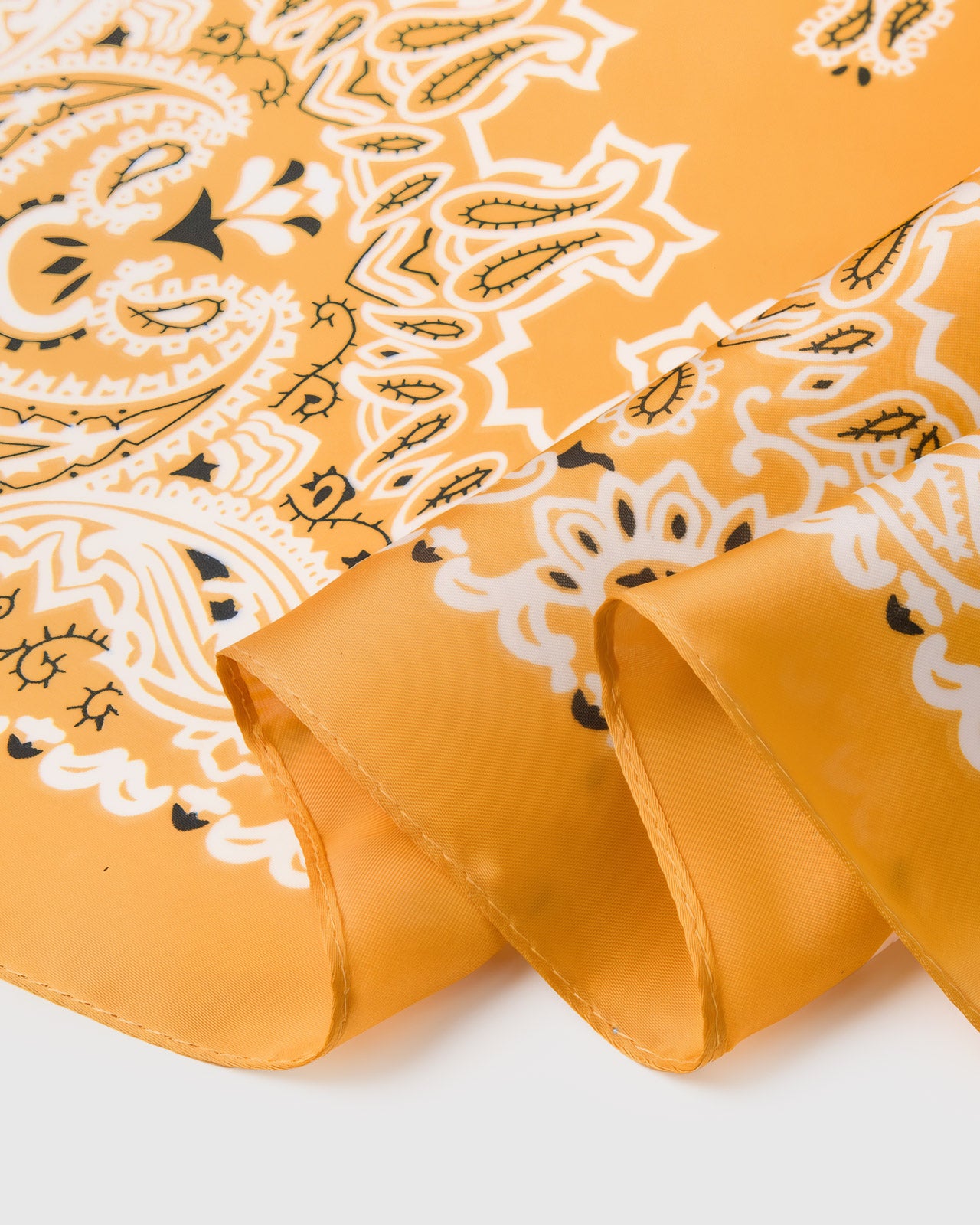 Close-up of the hand-illustrated paisley bandana corners printed in archival ivory and black on saffron silk