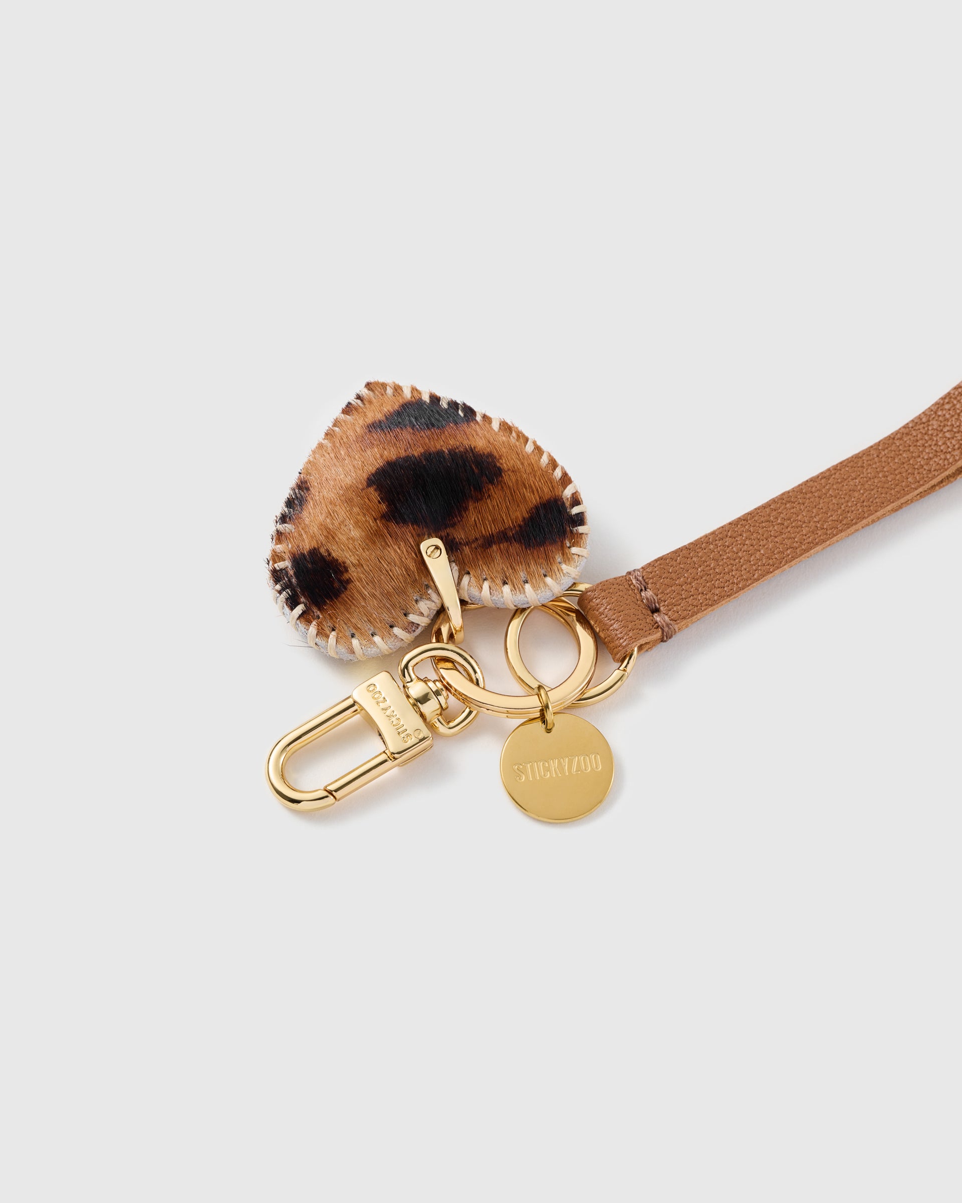 Close-up of the STICKYZOO leopard calf-hair heart charm, hand whip-stitched edge and hand-cut cognac leather