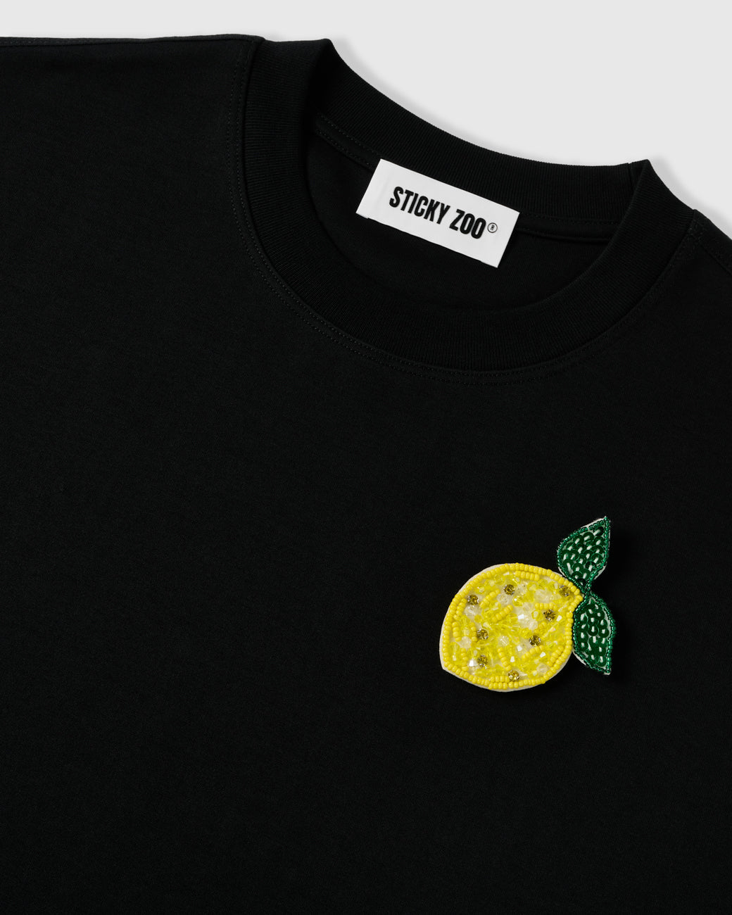 Raised, light-catching beadwork on the STICKYZOO Lemon T-Shirt lemon appliqué near the ribbed crew neck