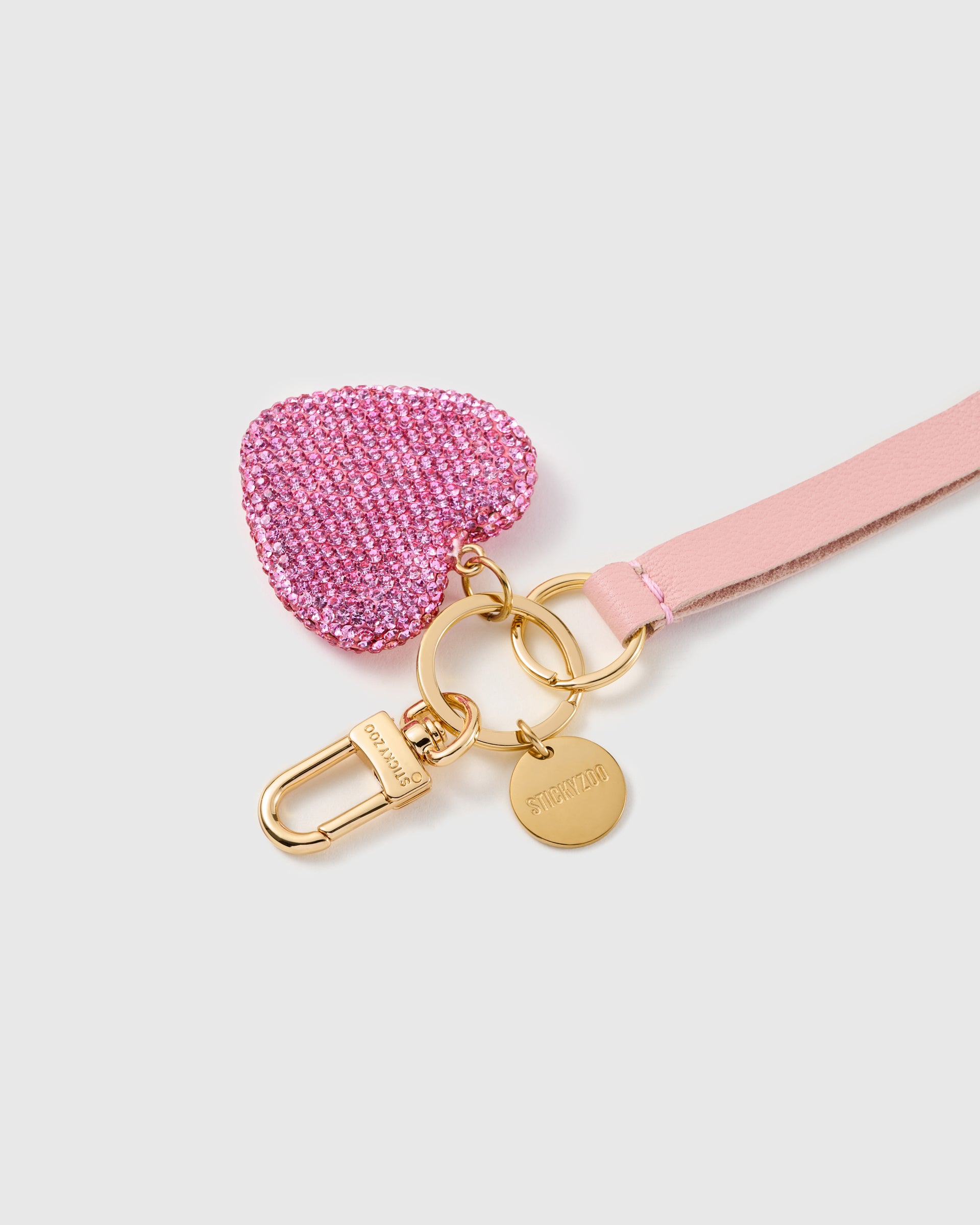 Blush crystal heart leather phone strap clipped to a phone case showing the hands-free wrist loop in use