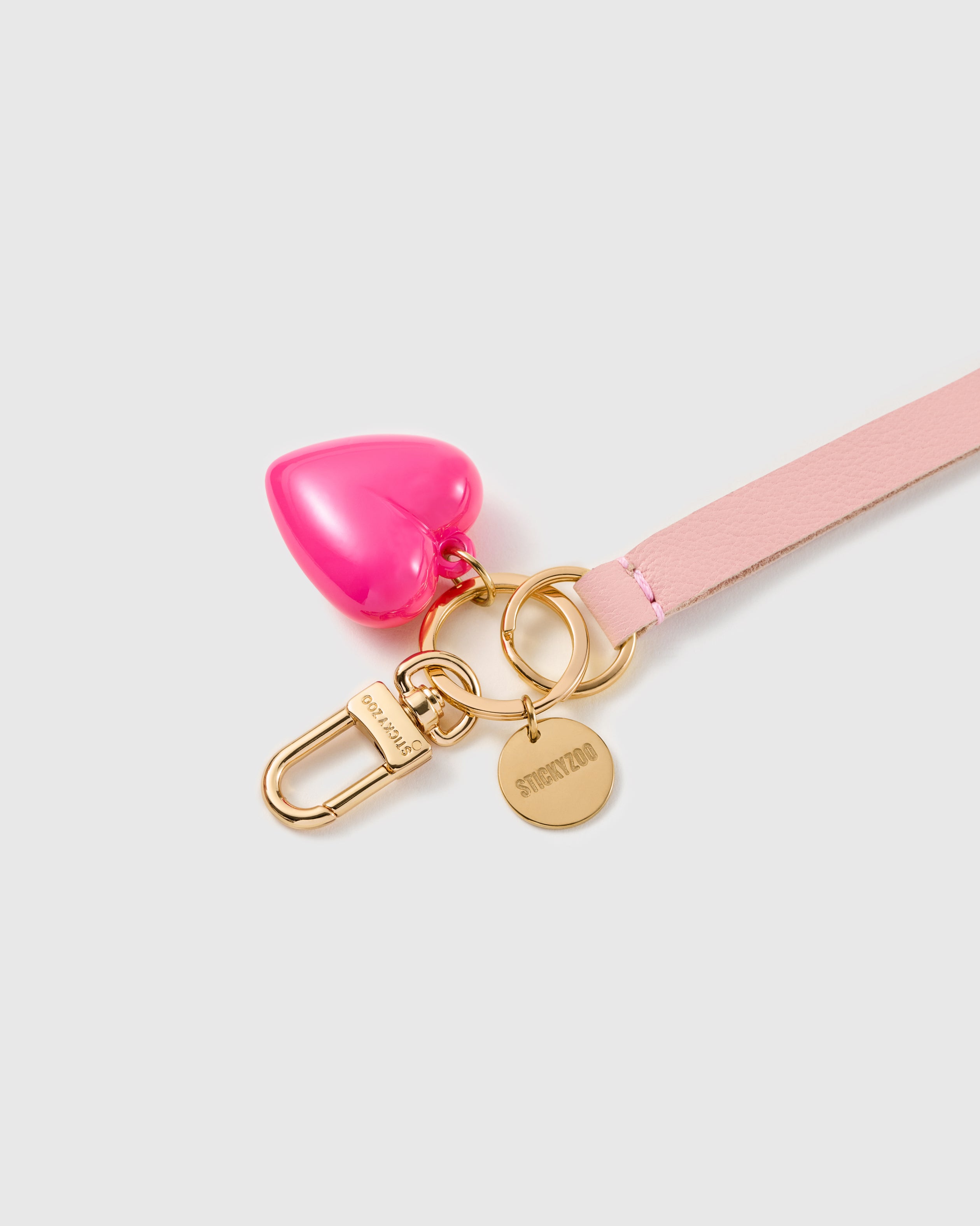 Blush puff heart leather phone strap clipped to a phone case showing the hands-free wrist loop in use