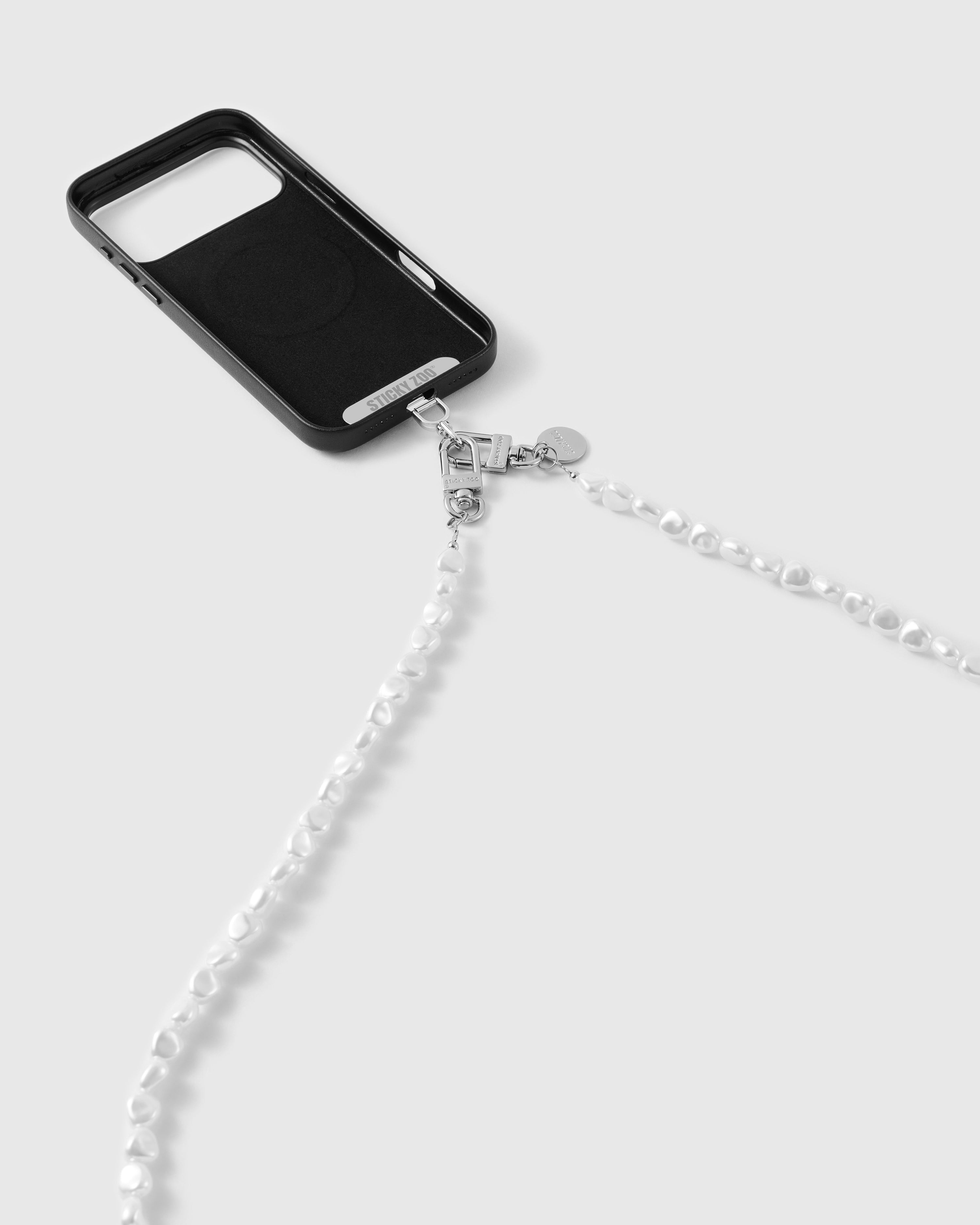 White faux-pearl phone strap clipped to a black case by silver-tone dual clasps and a round disc, strap trailing down the frame.