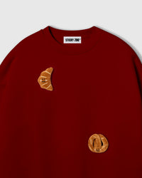 Close-up of crescent plush croissant with smiley face on red cotton showing golden-brown layered texture