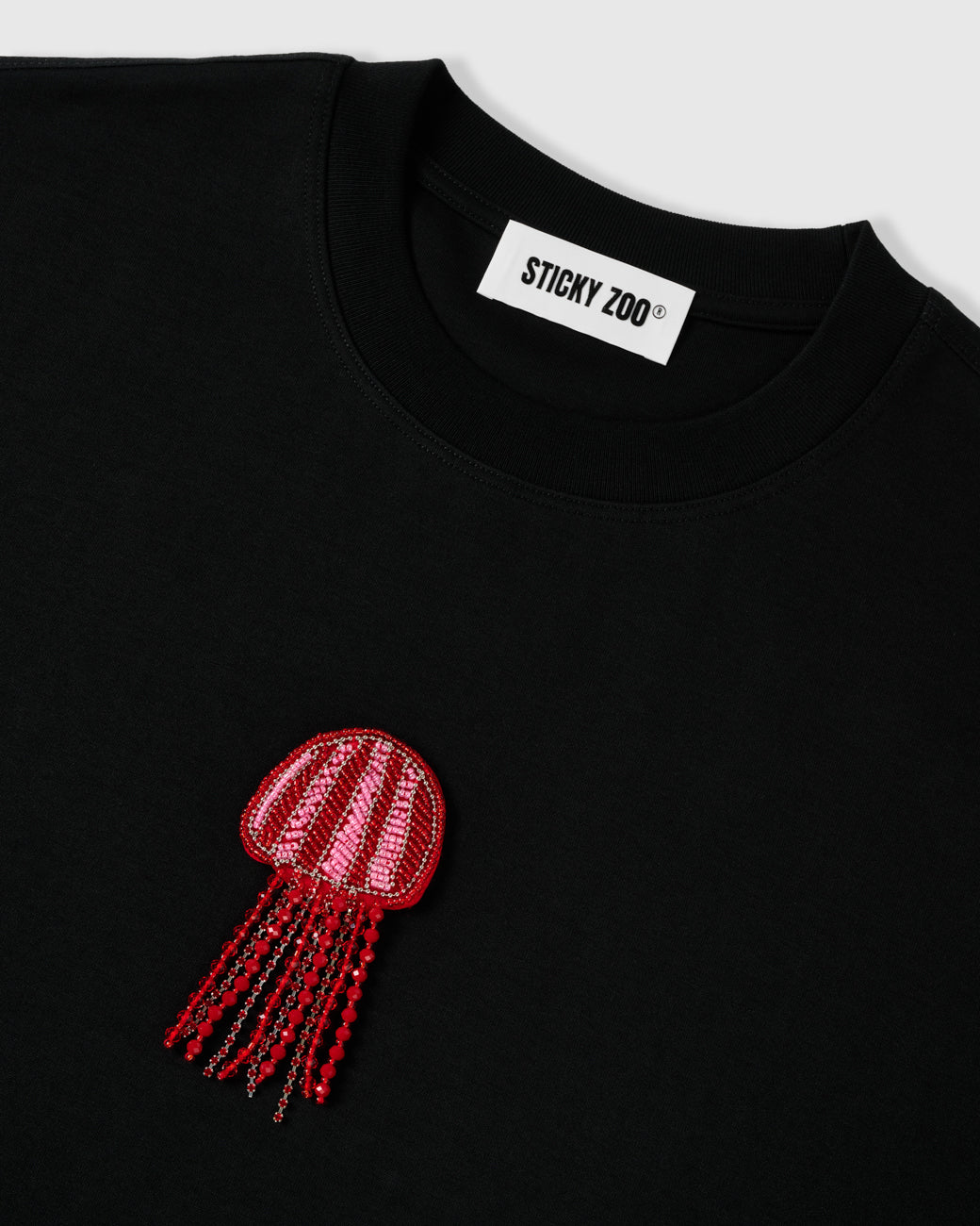 Beaded jellyfish appliqué below the STICKYZOO woven neck label on the black cotton tee showing the striped sequin bell and bead detail
