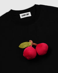 Angled close-up of hand-stitched cherry plush showing dimensional depth and soft sculpted surface