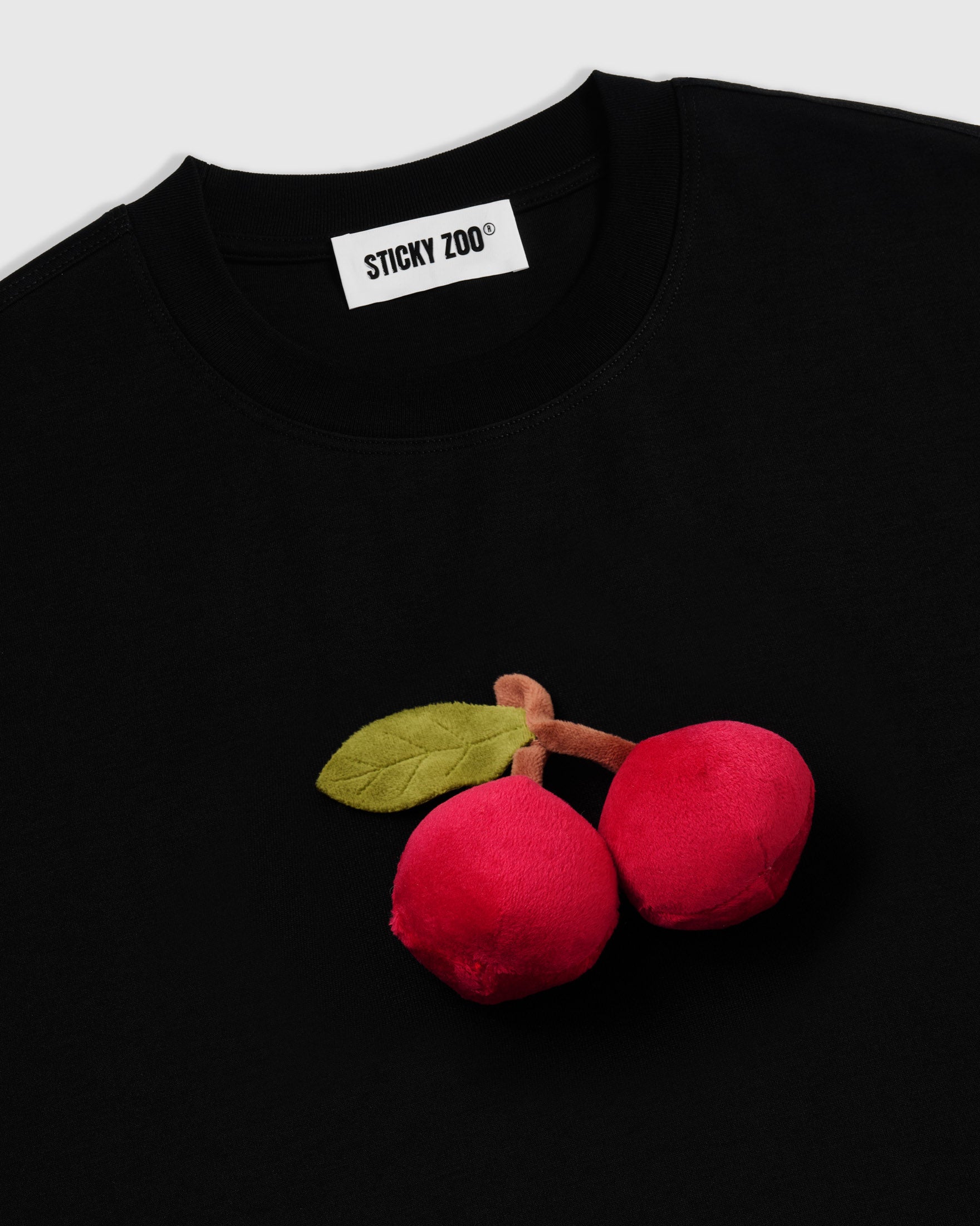 Angled close-up of hand-stitched cherry plush showing dimensional depth and soft sculpted surface
