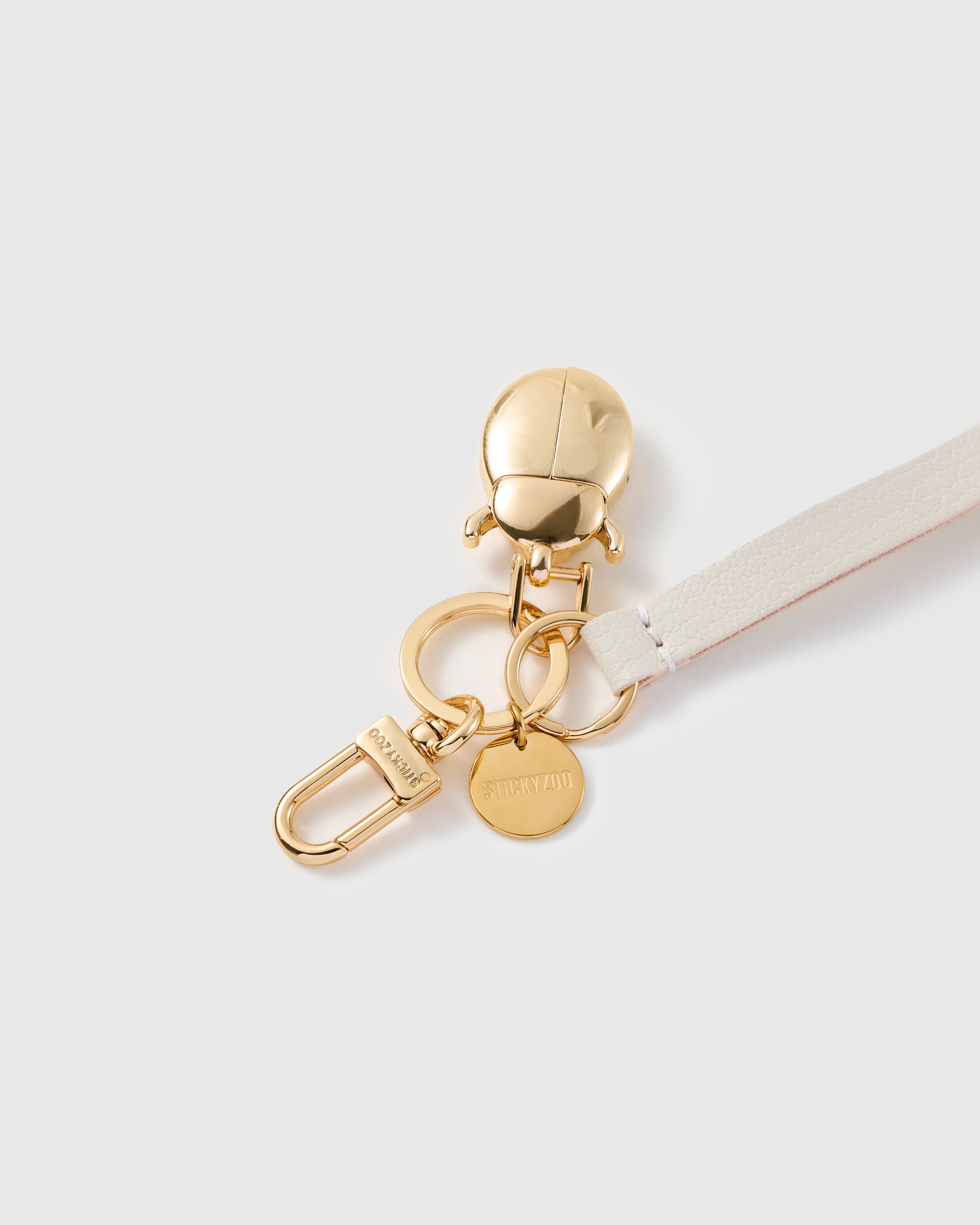 Golden ladybug leather phone strap close-up — sculpted gold-plated beetle charm and STICKYZOO engraved hook