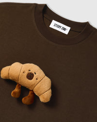 Close-up of neckline on STICKYZOO brown Runaway Croissant T-Shirt showing plush croissant and brand label