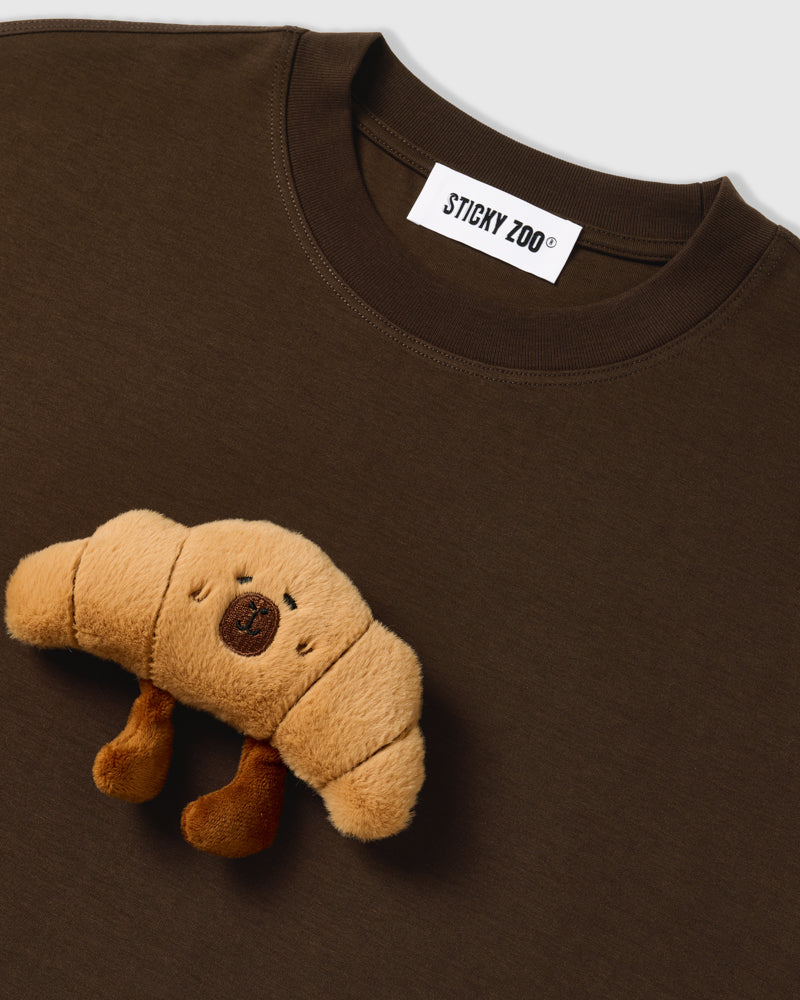 Close-up of neckline on STICKYZOO brown Runaway Croissant T-Shirt showing plush croissant and brand label