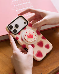 STICKYZOO jam heart phone case held in two hands above a pink hardcover book