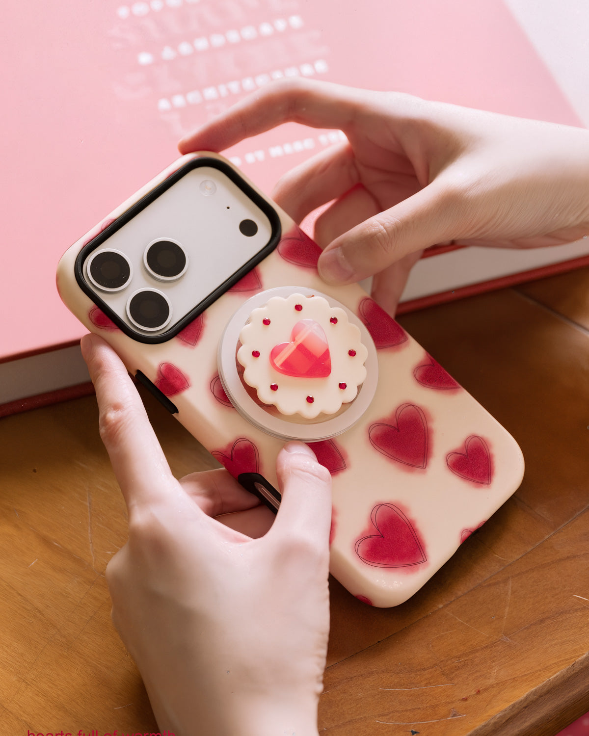 STICKYZOO jam heart phone case held in two hands above a pink hardcover book