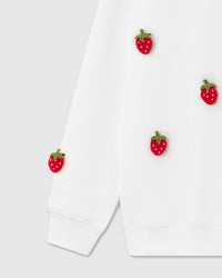 Close-up of plush strawberries on lower front and sleeve cuff on cream cotton showing placement