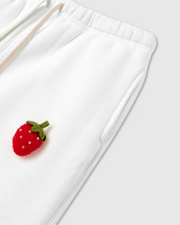Close-up of hand-stitched 3D plush strawberry at hip showing stuffed texture and green stem on white cotton
