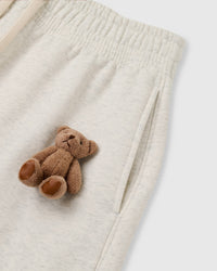 Close-up of plush teddy bear at hip on light gray heather fleece showing dimensional hand-sewn construction