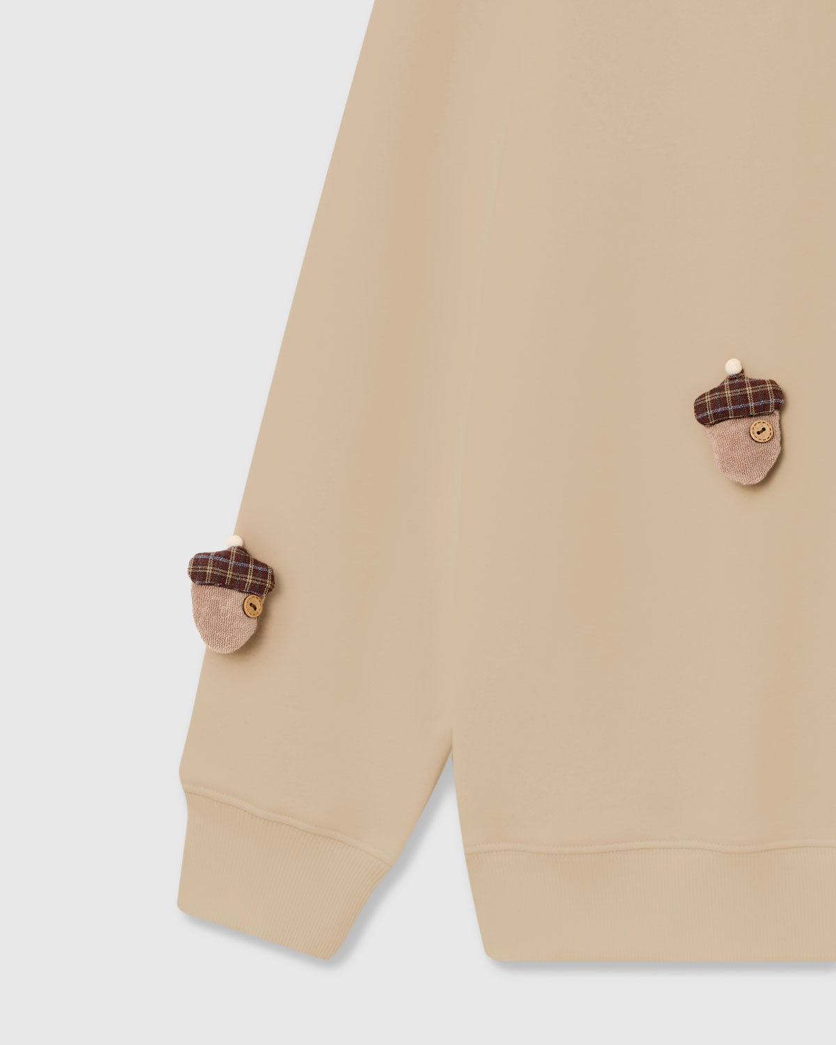 Detail of tartan-capped plush acorn applique with button center on cream cotton sweatshirt
