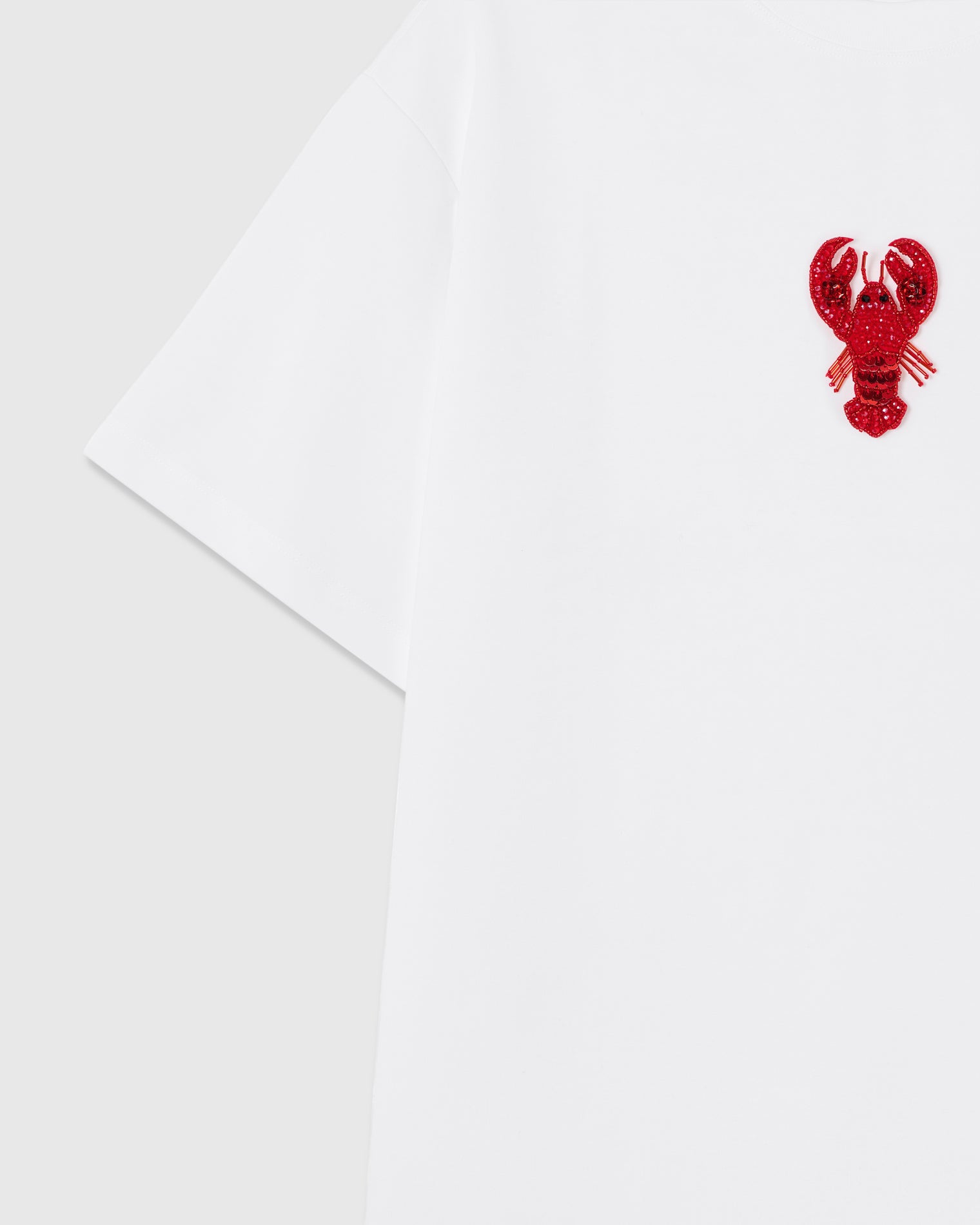 Detail of the raised lobster applique near the shoulder showing sequin tail scales and beaded antennae sewn onto white cotton.
