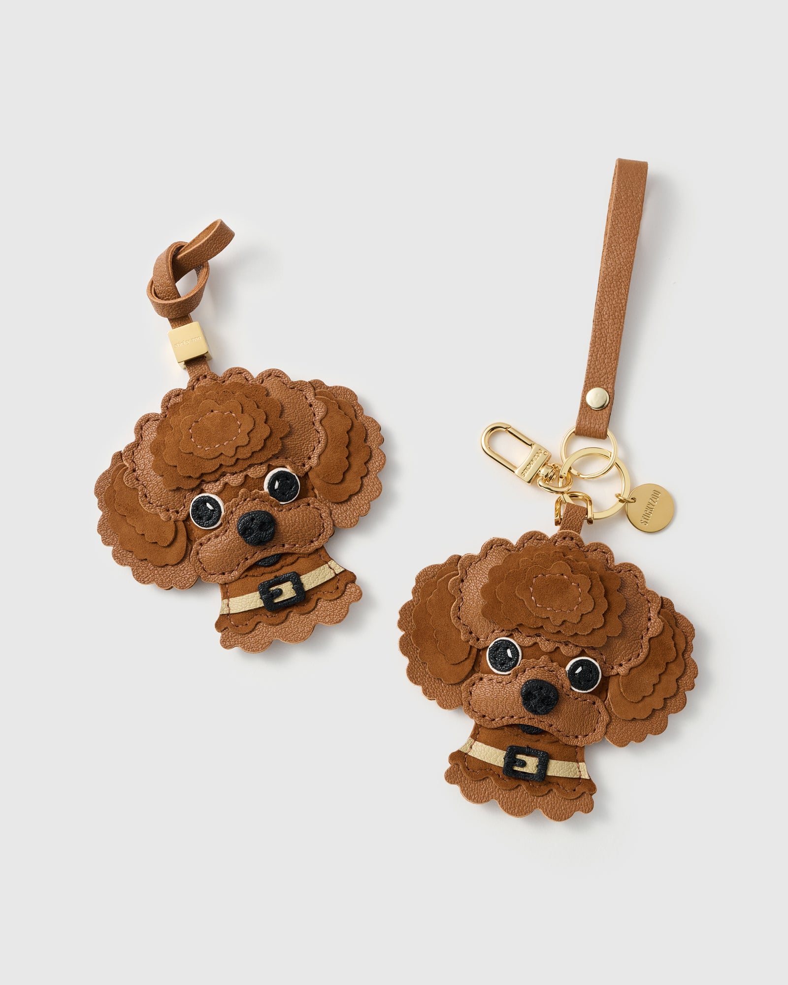 {{Dual attachment.}} Both editions of The Poodle Charm — leather strap loop for bags, or 18K gold-plated keychain clip with engraved STICKYZOO disc.