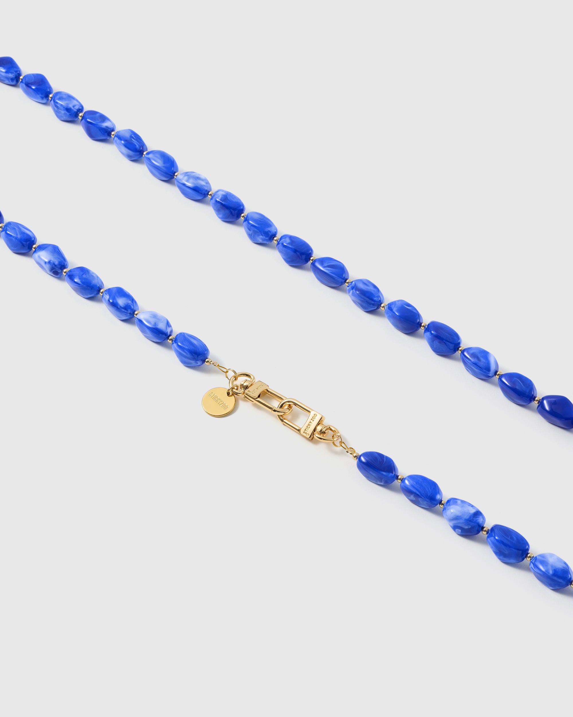 Macro close-up of polished cobalt resin nugget beads and gold-plated clasp on a handmade STICKYZOO strap