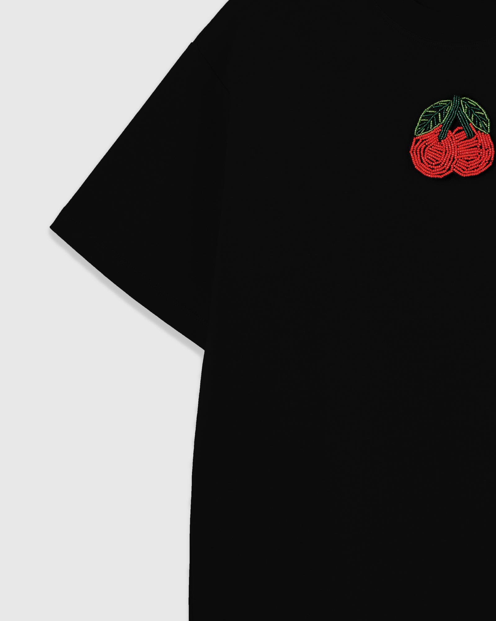 STICKYZOO Cherry T-Shirt close-up showing the raised glass seed bead cherry motif on the upper chest with dropped shoulder and short sleeve