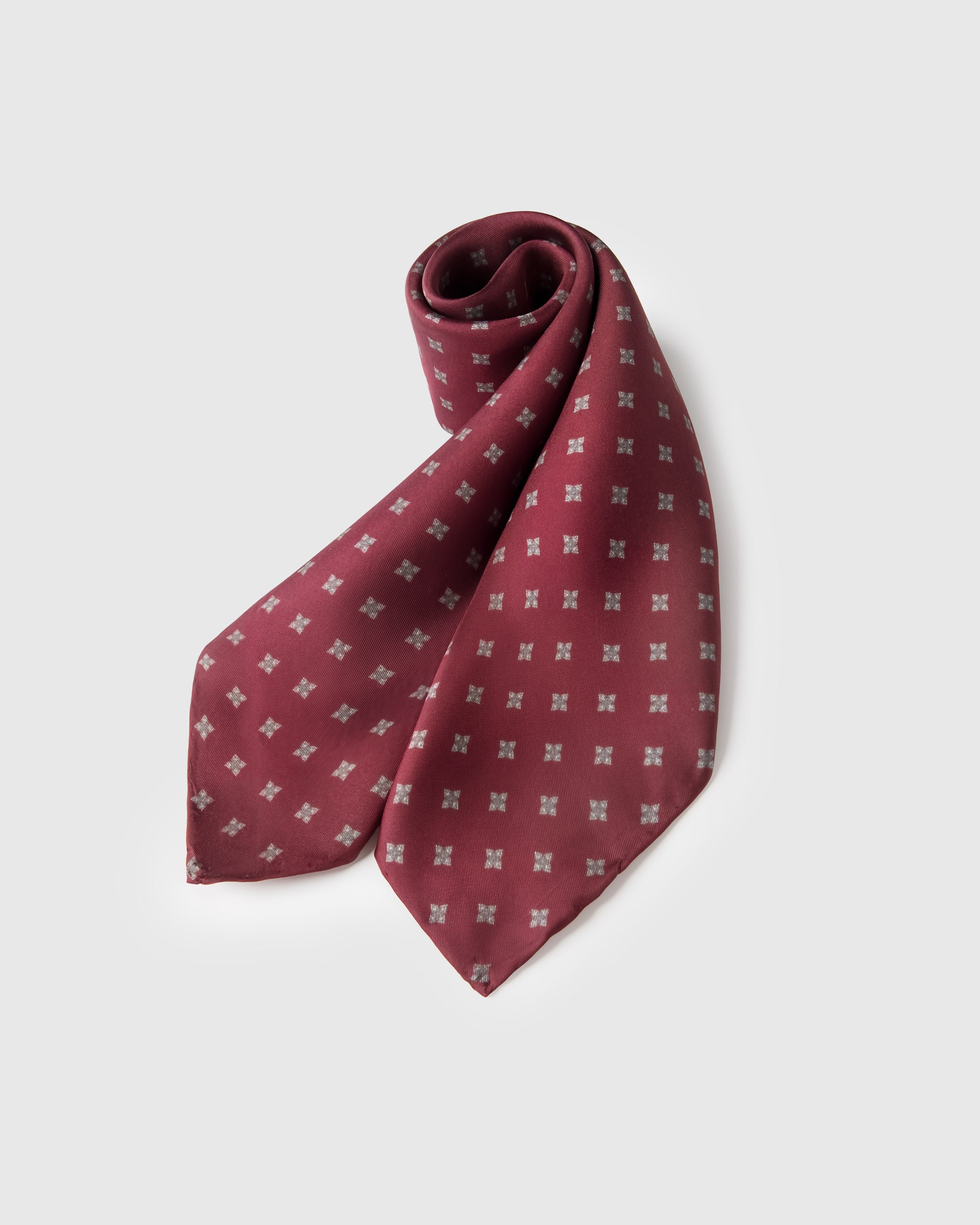 Burgundy foulard silk scarf rolled to show the print across the silk and the considered grid
```