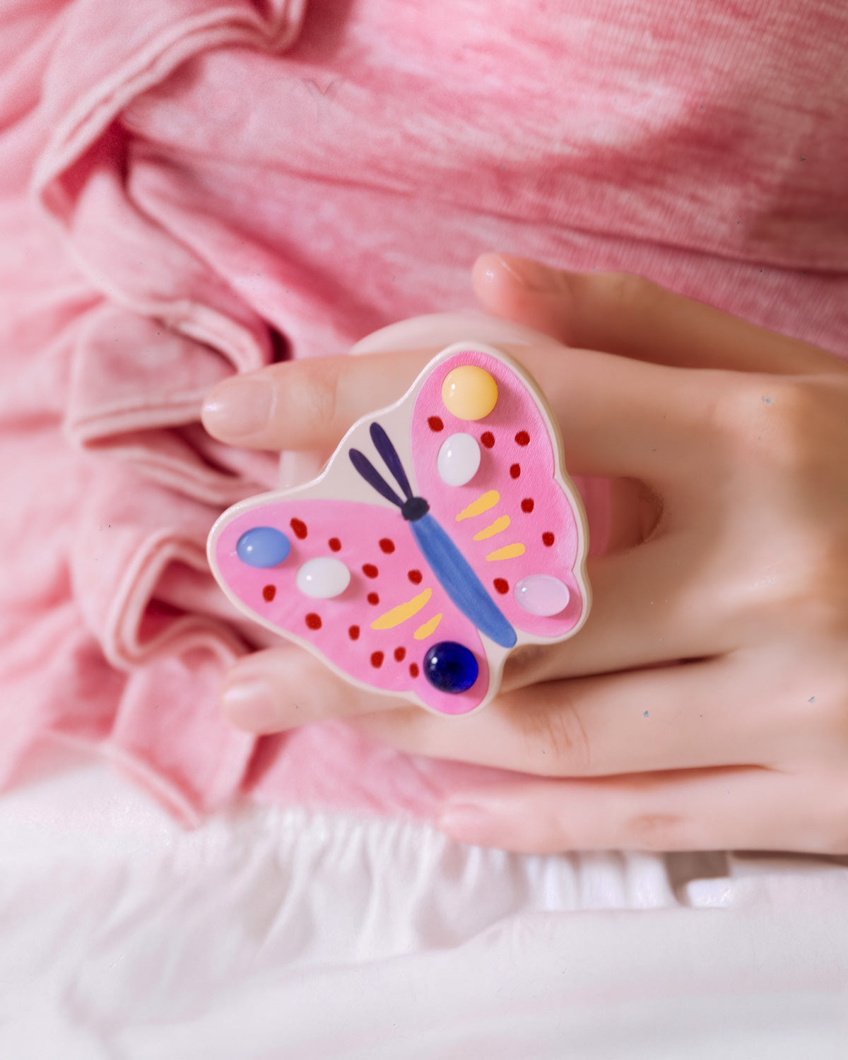 STICKYZOO painted butterfly grip held in hand, with jewel-tone gem dots set across the resin wings