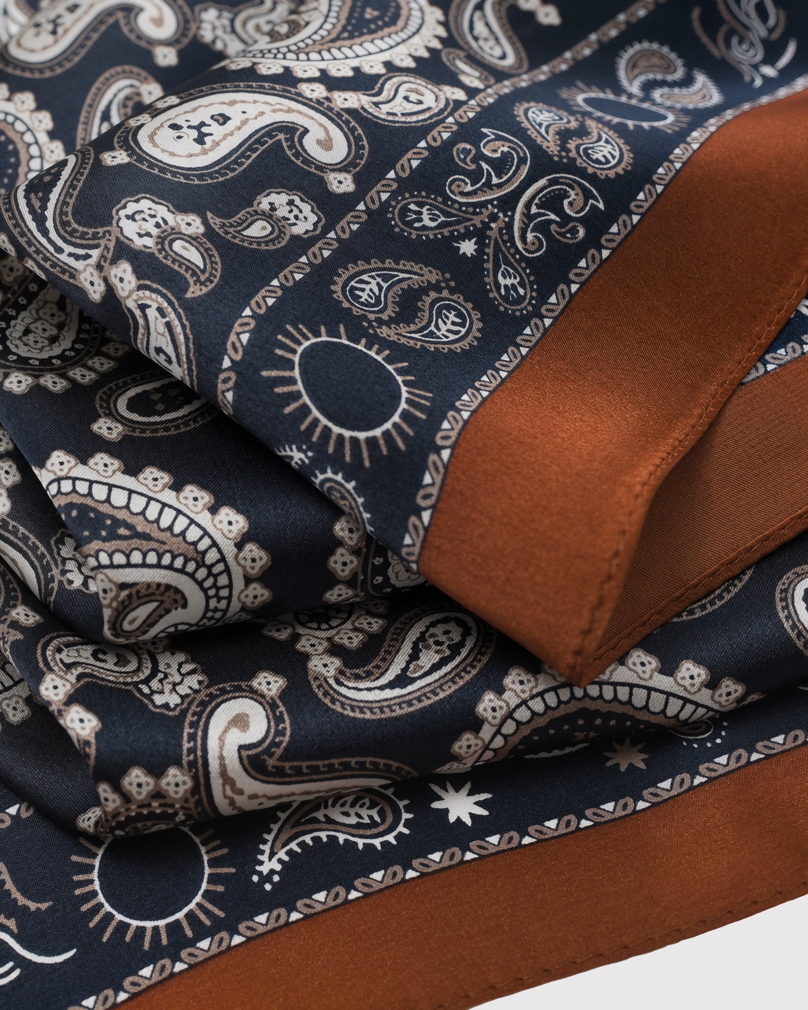Cognac border meets the navy paisley field showing the silk drape and printed motif detail
```