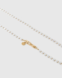 Close-up of irregular white faux-pearls and small gold-tone beads meeting the gold dual clasp and round engraved disc.