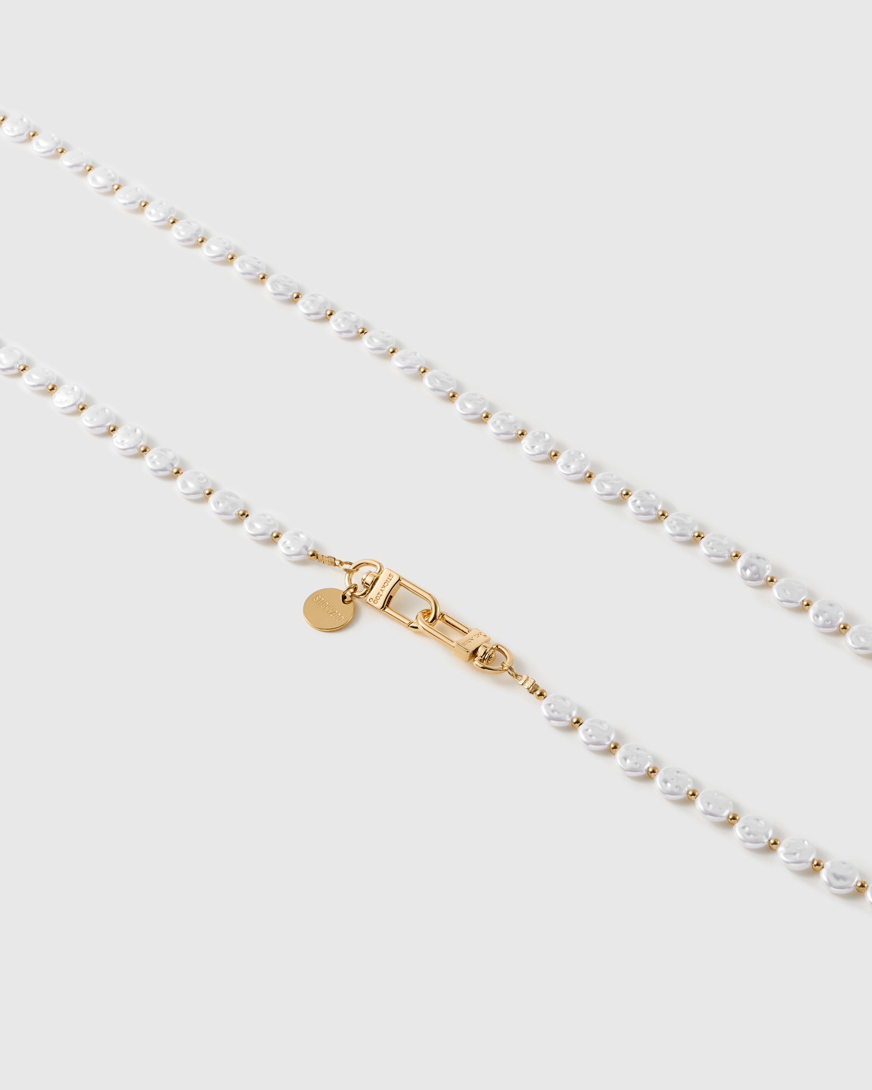 Close-up of irregular white faux-pearls and small gold-tone beads meeting the gold dual clasp and round engraved disc.