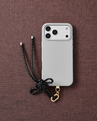 Phone with black leather bow strap on dark brown fabric lifestyle flat-lay