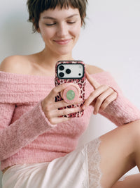 Phone gripped with fingers around the popped MagSafe grip on the rose leopard case in daily use