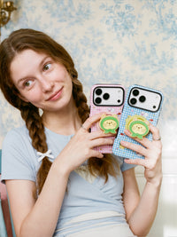Two STICKYZOO green-hood cat phone cases in pink and blue held up, showing the built-in MagSafe grip on each.