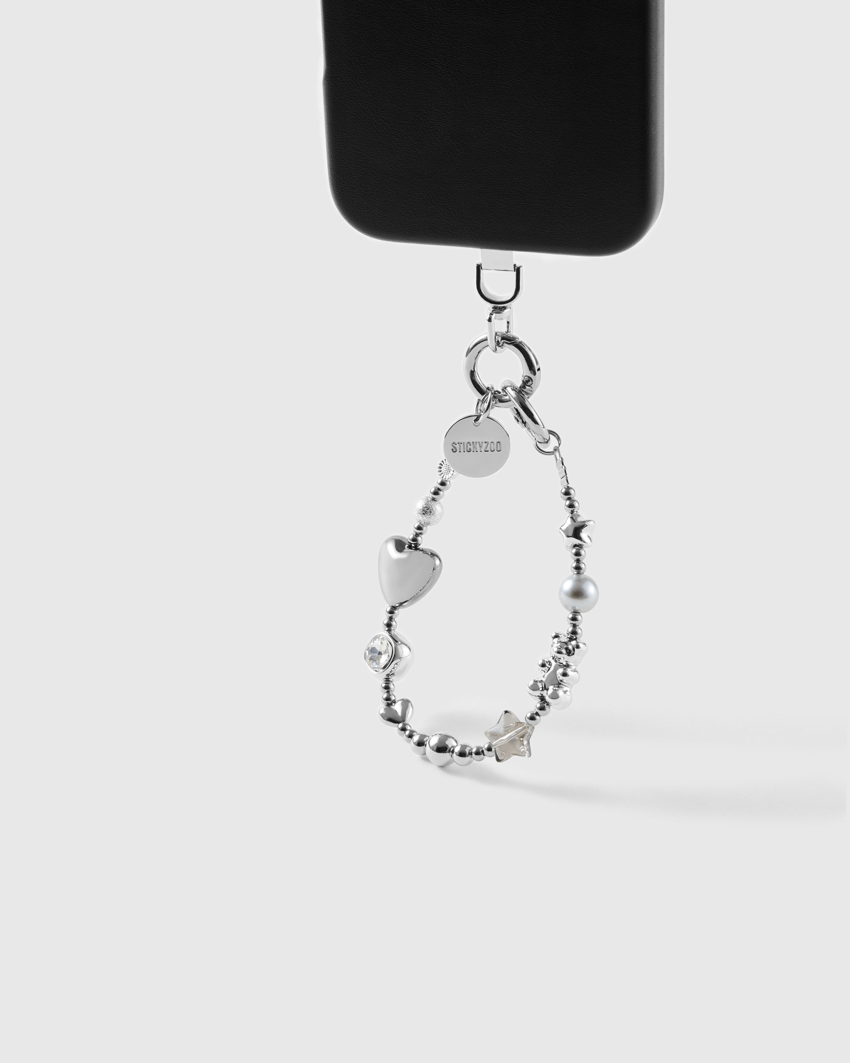 Silver beaded wrist strap hanging from a black phone case, silver puff heart, grey pearl-effect bead, star beads and STICKYZOO disc in the loop
