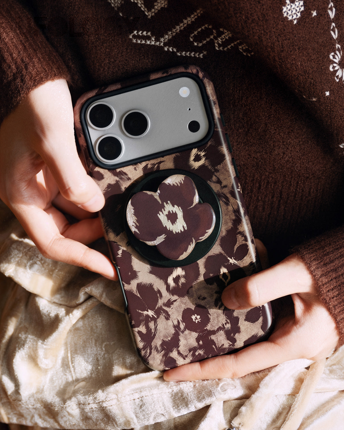 Phone held with fingers around the popped-out poppy grip on the back of the burgundy case
