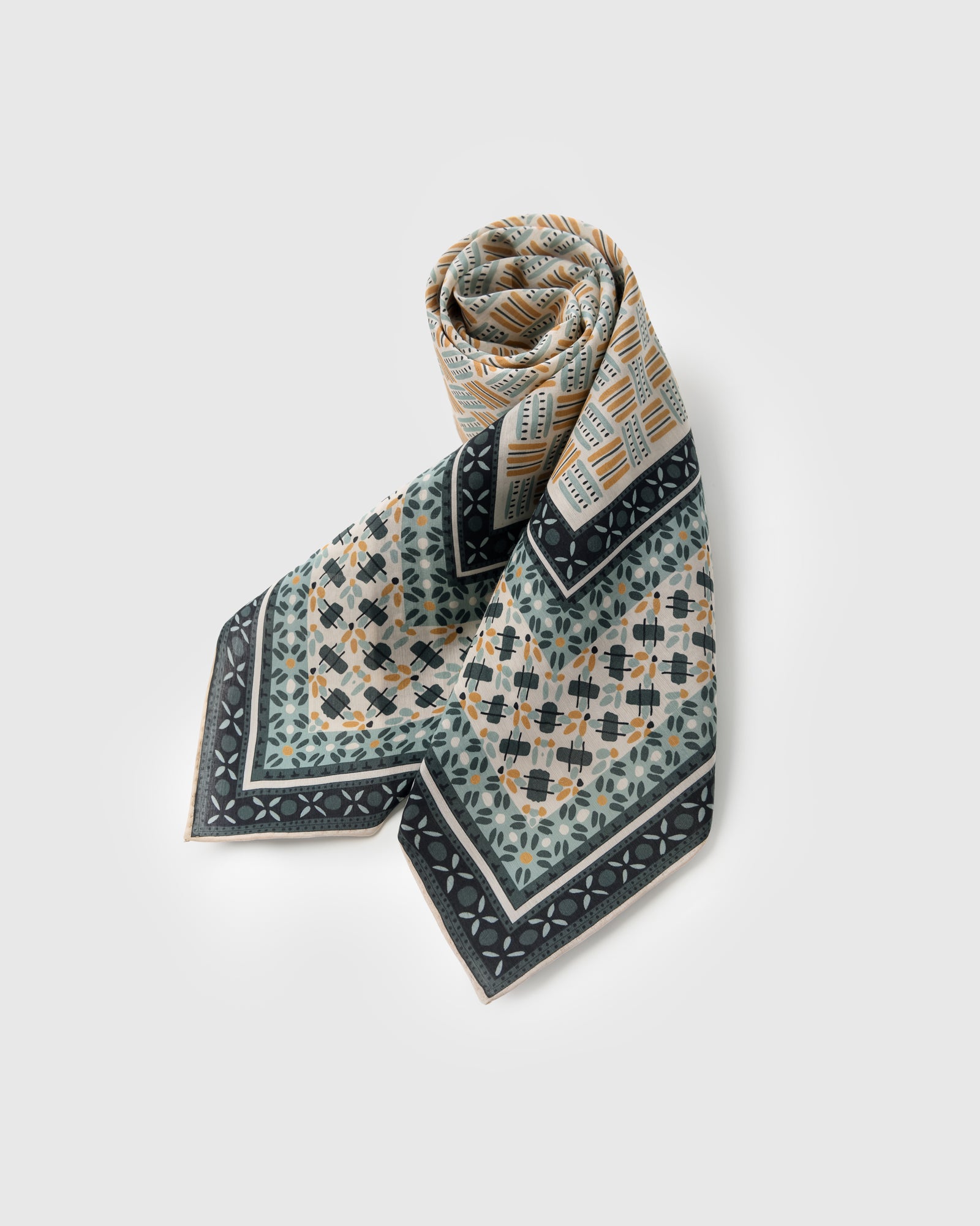Mosaic silk scarf rolled to show the saffron and sage tile tessellation and the soft drape
```