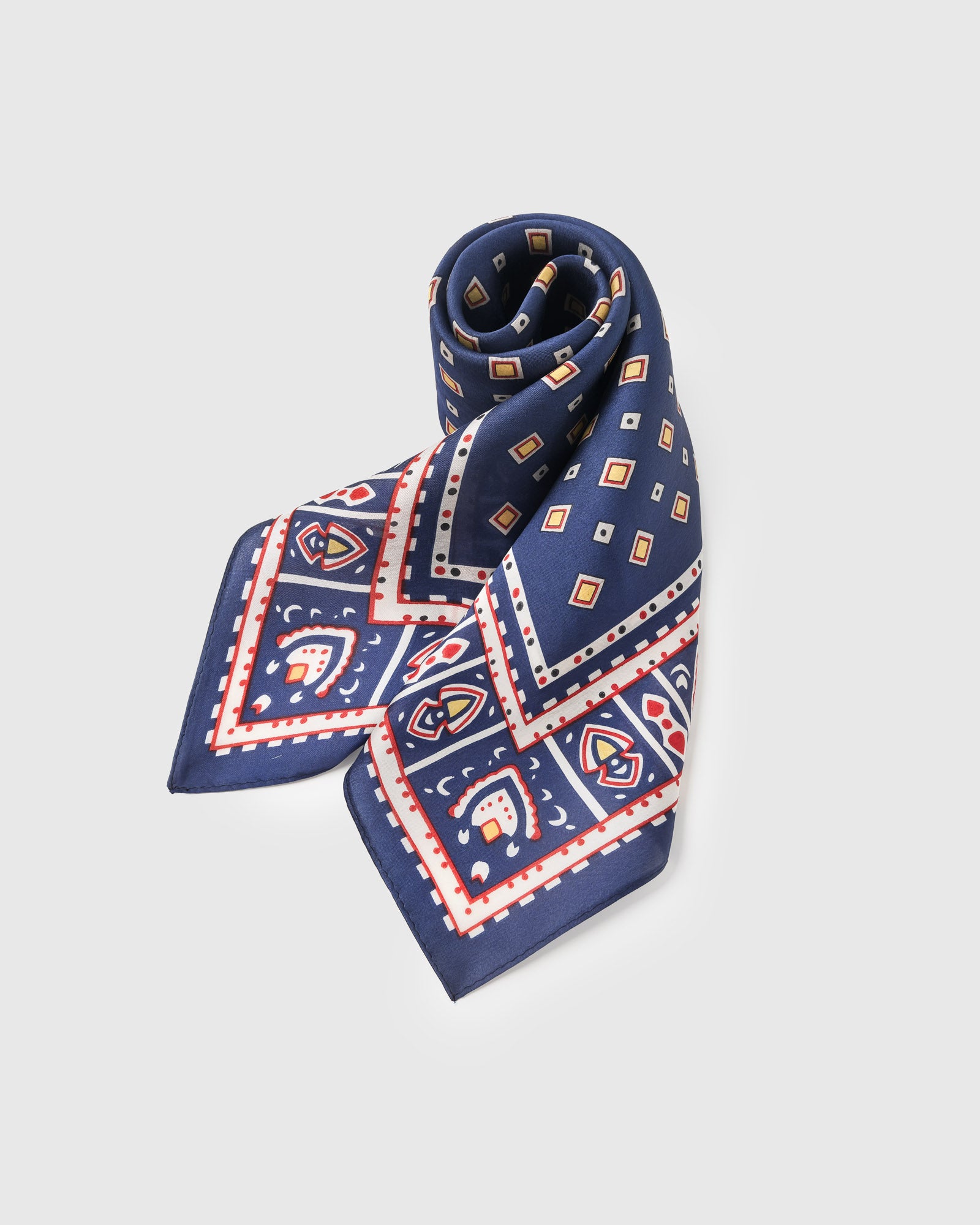 Navy silk foulard scarf rolled into a soft fold showing the diamond field and ornate border
```