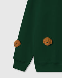 Detail view of hand-stitched poodle faces on green cotton showing 3D plush depth and individual character