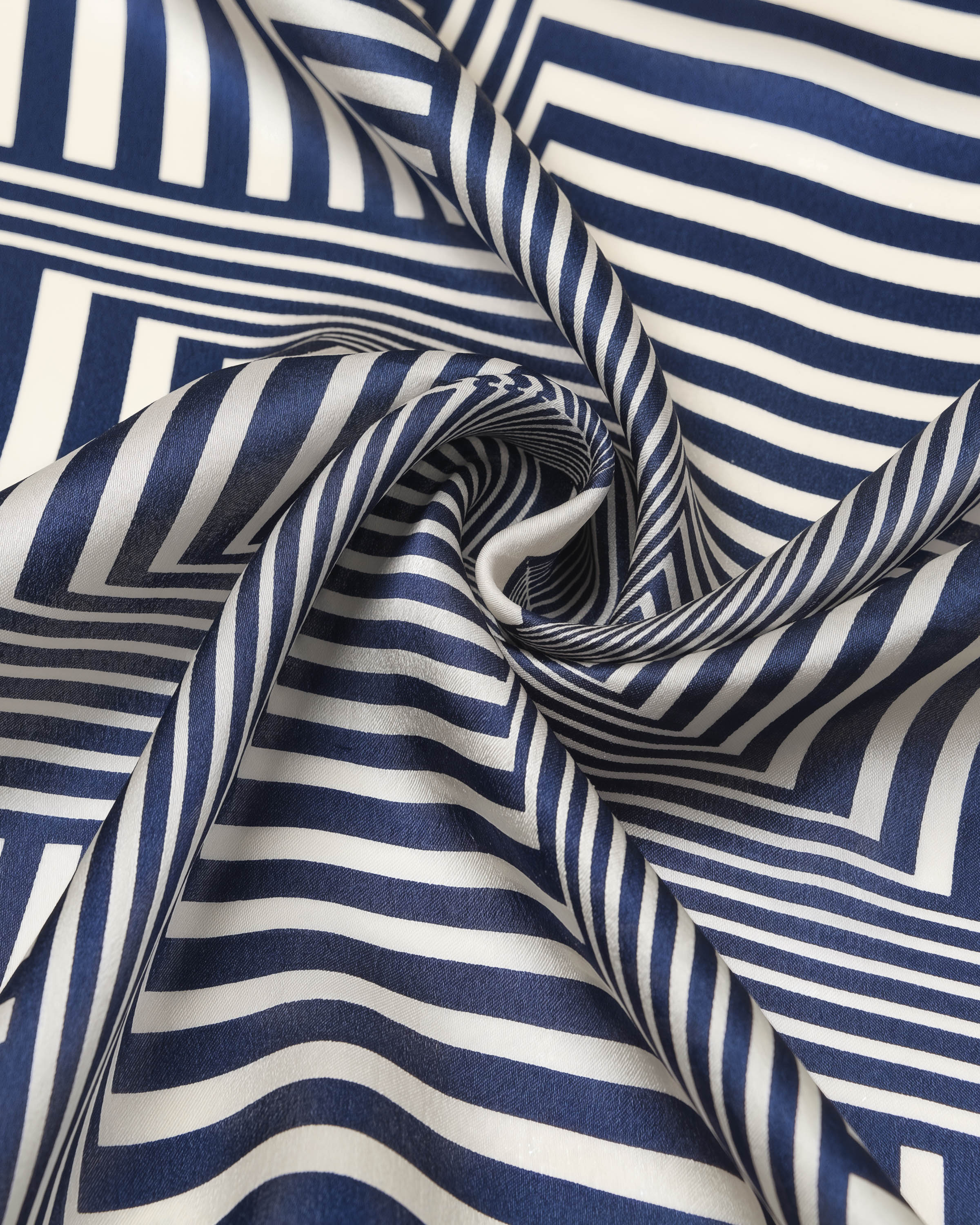 Silk scarf coiled to show the soft drape of the optical-stripe print and the ivory border catching light
```