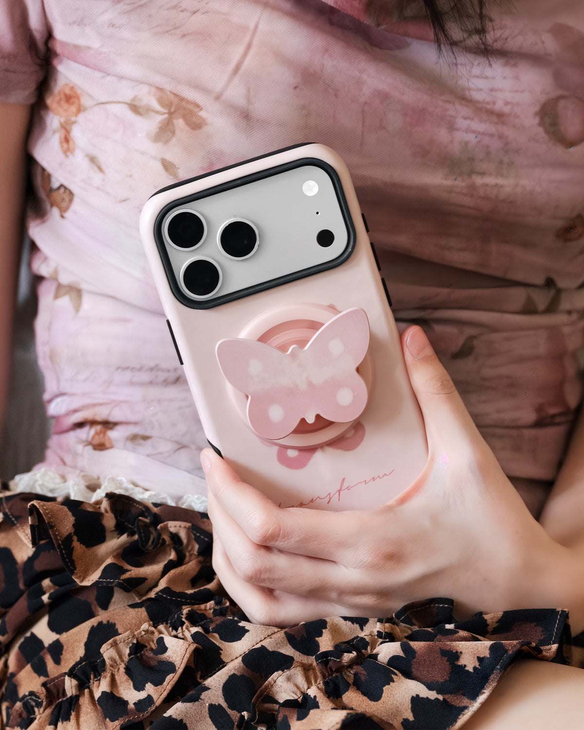 Pearl butterfly phone case held against a soft floral dress with the popped-out MagSafe butterfly grip on the back